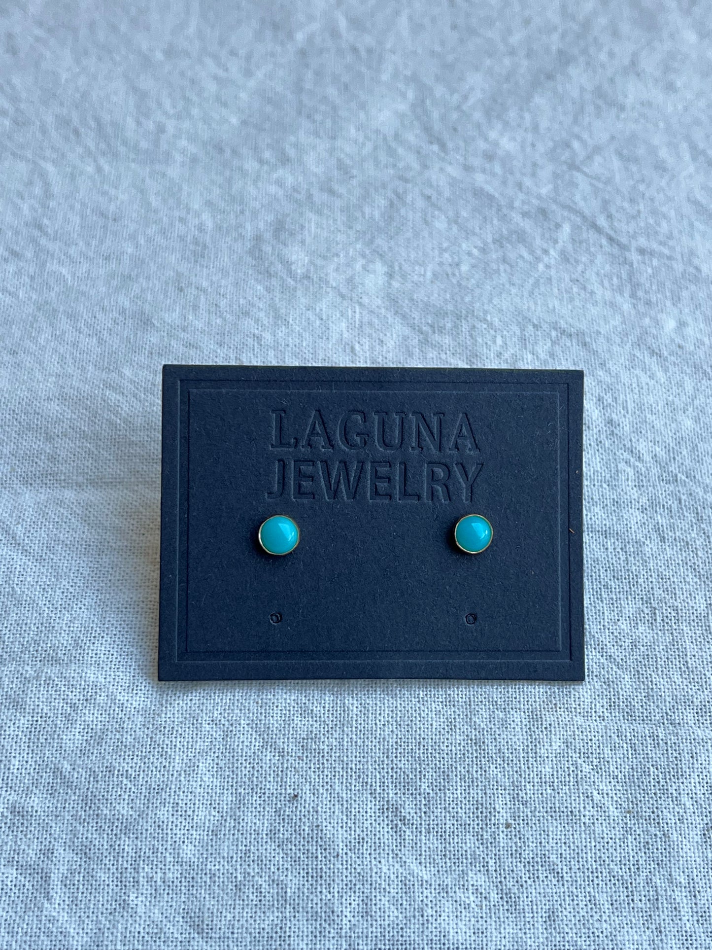 Image of small gold filled studs with turquoise stones on black paper earring card against a white background